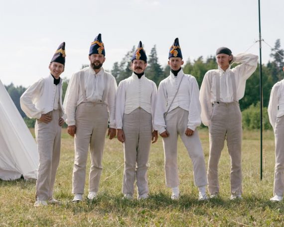 A group of soldiers in historical uniforms standing in a field beside a tent.