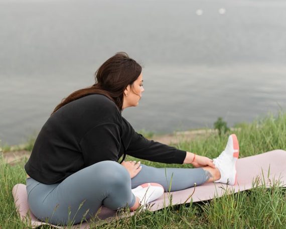 A woman stretches on a yoga mat by a serene lake, embodying relaxation and wellness in nature.