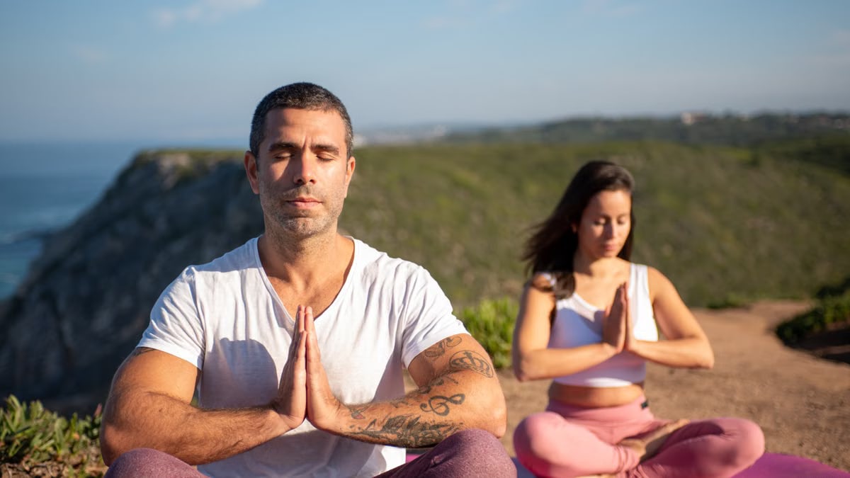 Man and woman meditating outdoors on yoga mats by the coast in Portugal.
